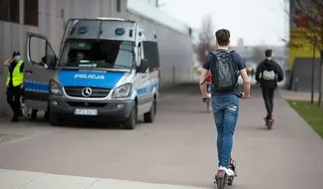 Mężczyzna na hulajnodze, w tle radiowóz policji