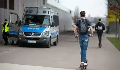 Mężczyzna na hulajnodze, w tle radiowóz policji
