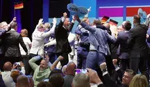 Uczestnicy wydarzenia AfD świętują na scenie z niemieckimi flagami i tablicami „Vision 2026 – Deutschland zuerst”.
